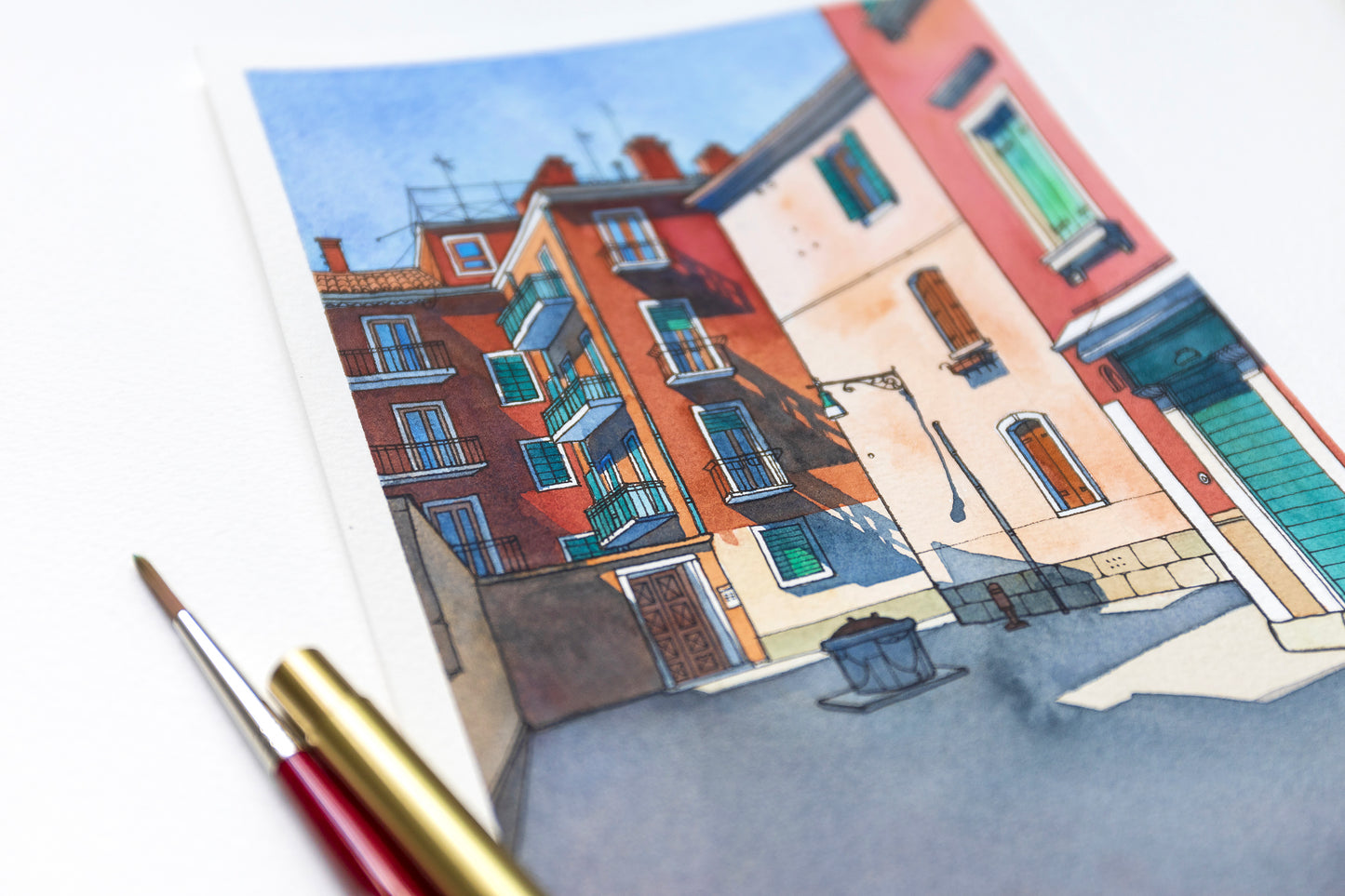 Close-up of original watercolor and ink illustration of Ramo de le Muneghe in Venice, Italy, with art supplies on a white background