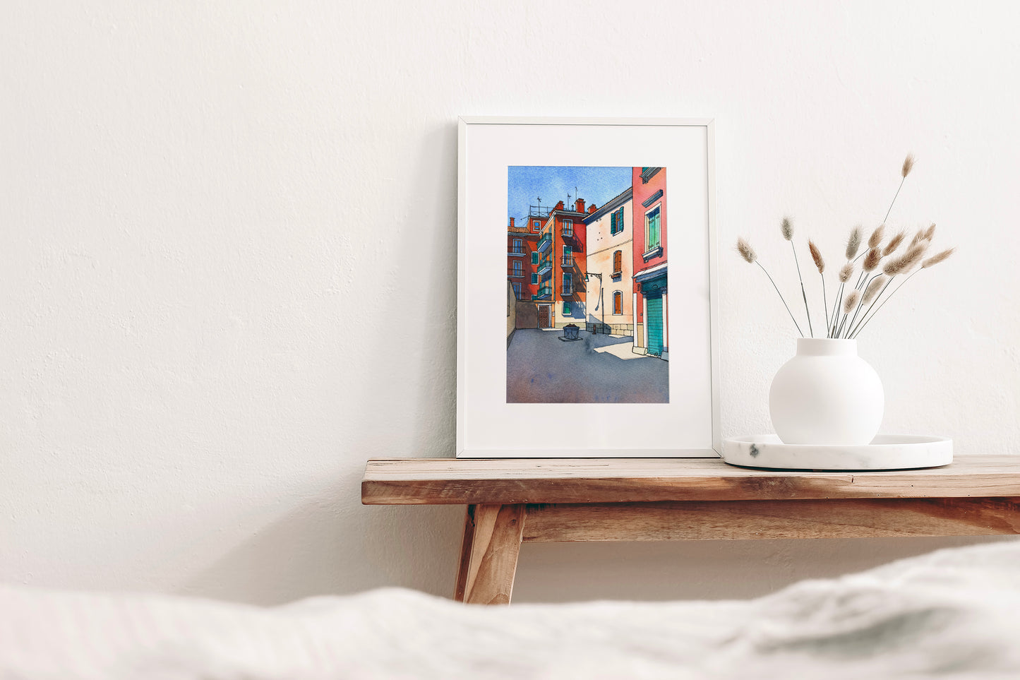 Framed watercolor artwork with Ramo de le Muneghe in Venice on a wooden shelf with a vase containing dried plants.