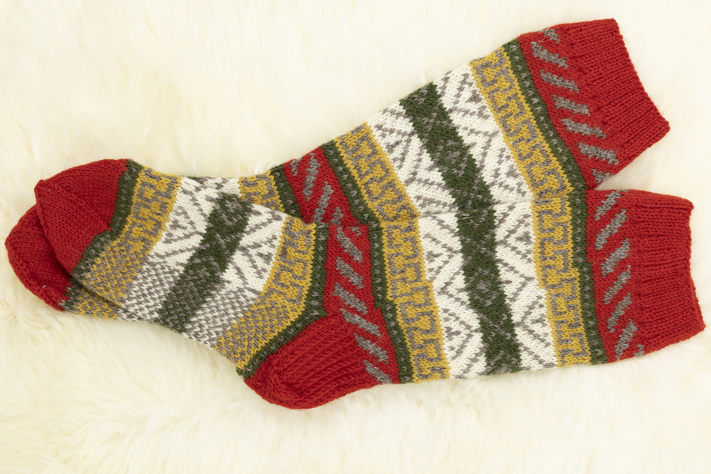 Pair of hand-knitted mid-calf wool socks with red, green, yellow and white geomertic pattern on a white background