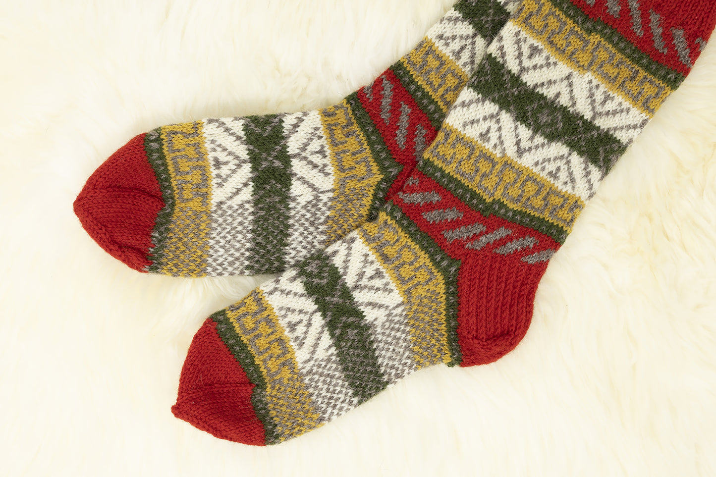 Close-up of a pair of hand-knitted mid-calf wool socks with red, green, yellow and white geomertic pattern on a white background