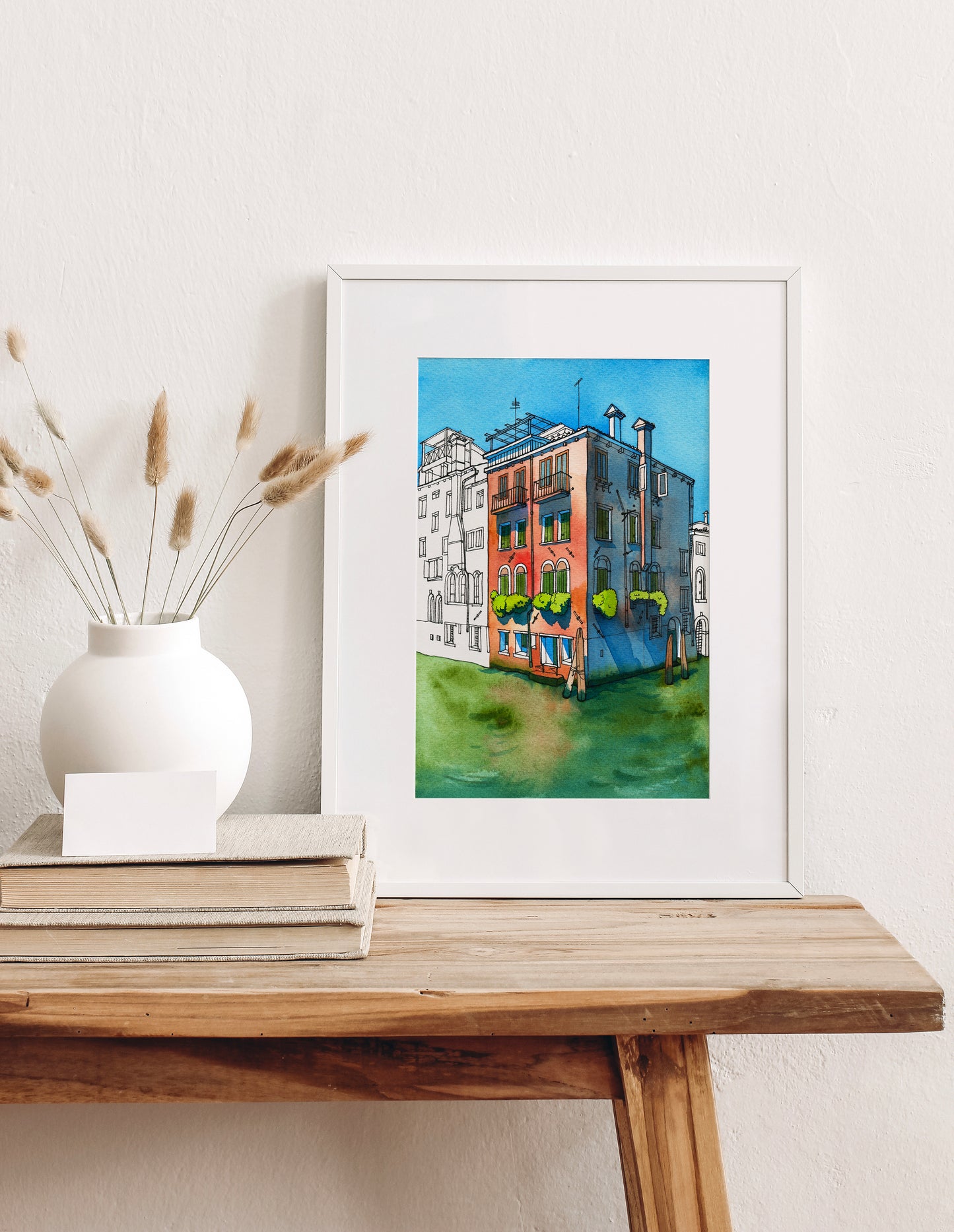 Framed artwork of a colorful historical building on Rio della Misericordia in Venice on a wooden table with decorative elements.