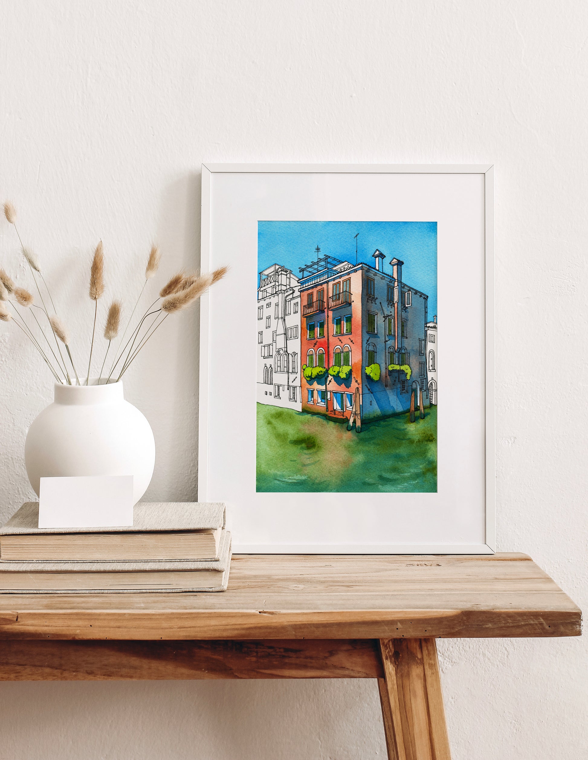 Framed artwork of a colorful historical building on Rio della Misericordia in Venice on a wooden table with decorative elements.