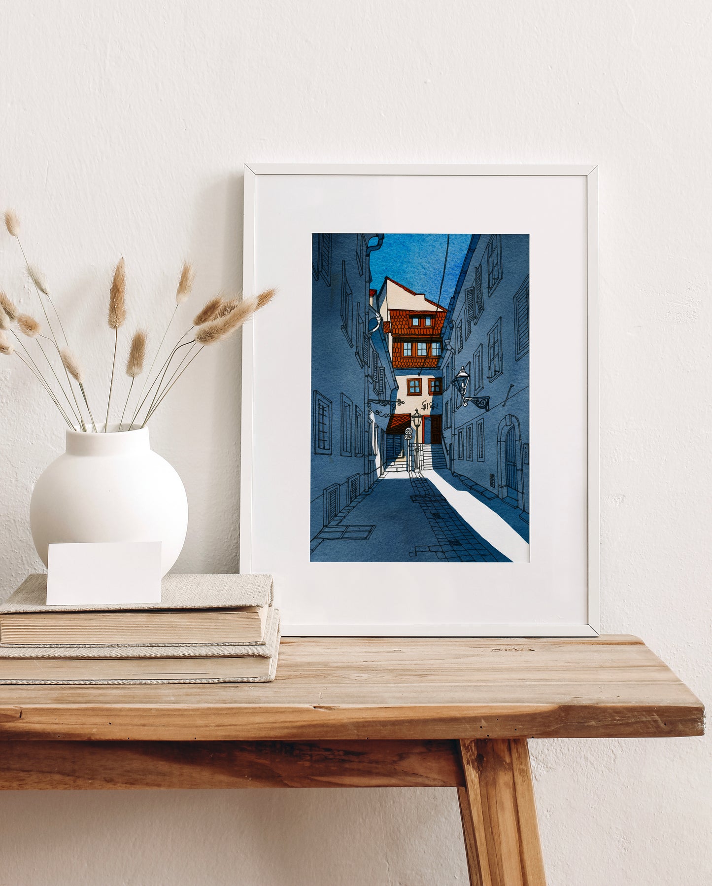 Framed watercolor and ink artwork, featuring narrow courtyard alley in Sackstrasse 40 in Graz, Austria, displayed on a wooden table with decorative items.