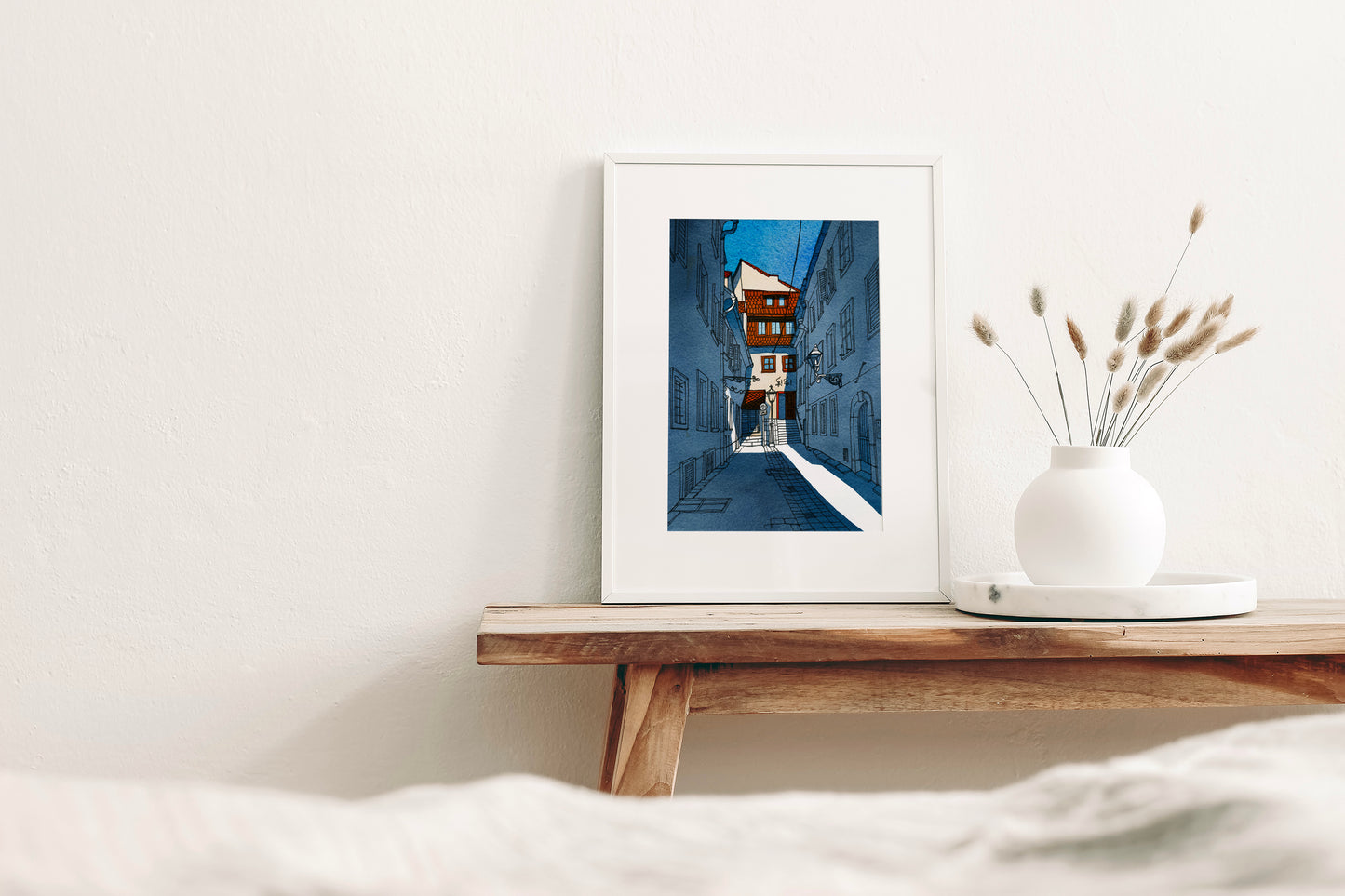 Framed watercolor and ink artwork, featuring narrow courtyard alley in Sackstrasse 40 in Graz, Austria, displayed on a wooden shelf with a vase containing dried plants.