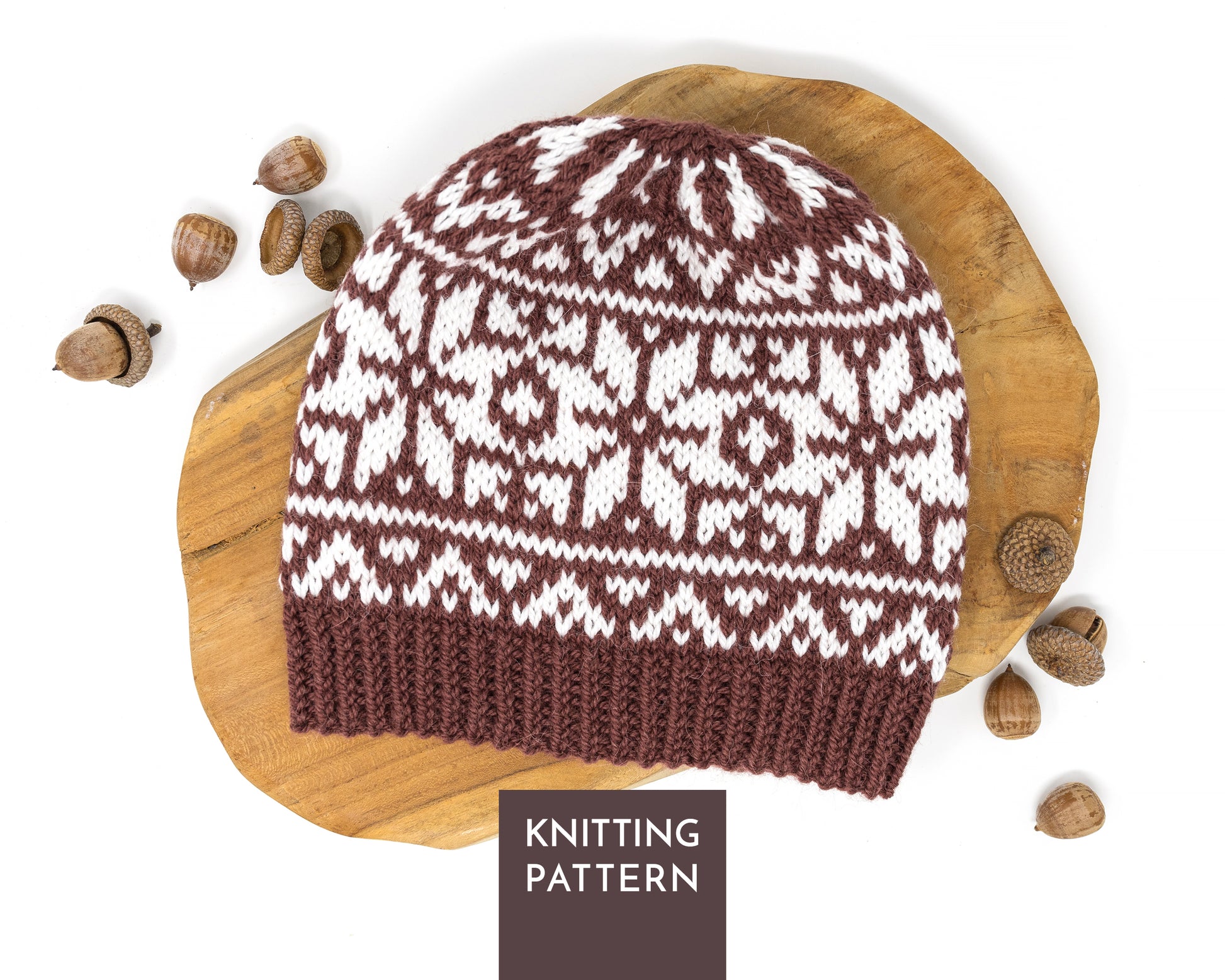 A knitted beanie hat with a brown and white Selburose pattern, displayed on a wooden slice with acorns, and a label reading 'KNITTING PATTERN' at the bottom.