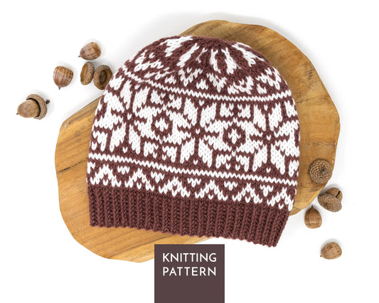 A knitted beanie hat with a brown and white Selburose pattern, displayed on a wooden slice with acorns, and a label reading 'KNITTING PATTERN' at the bottom.