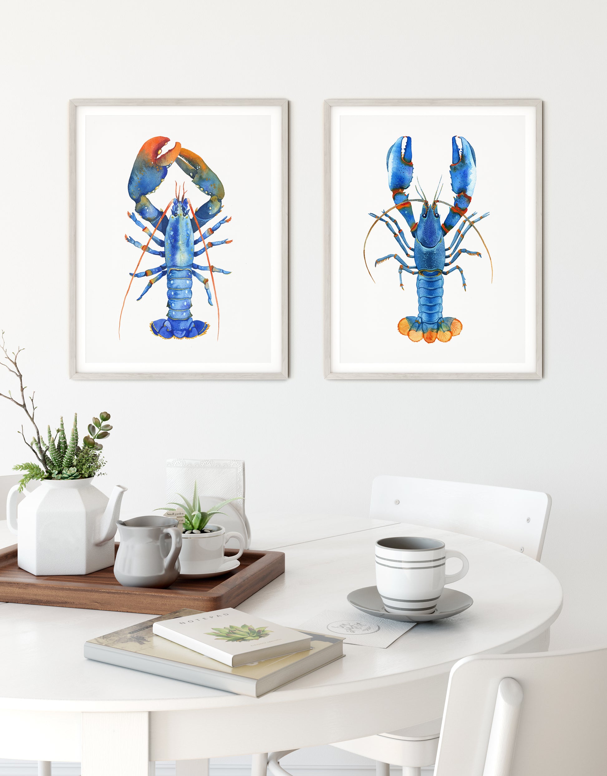 Set of two framed watercolor lobster prints hanging side-by-side on a kitchen white wall.