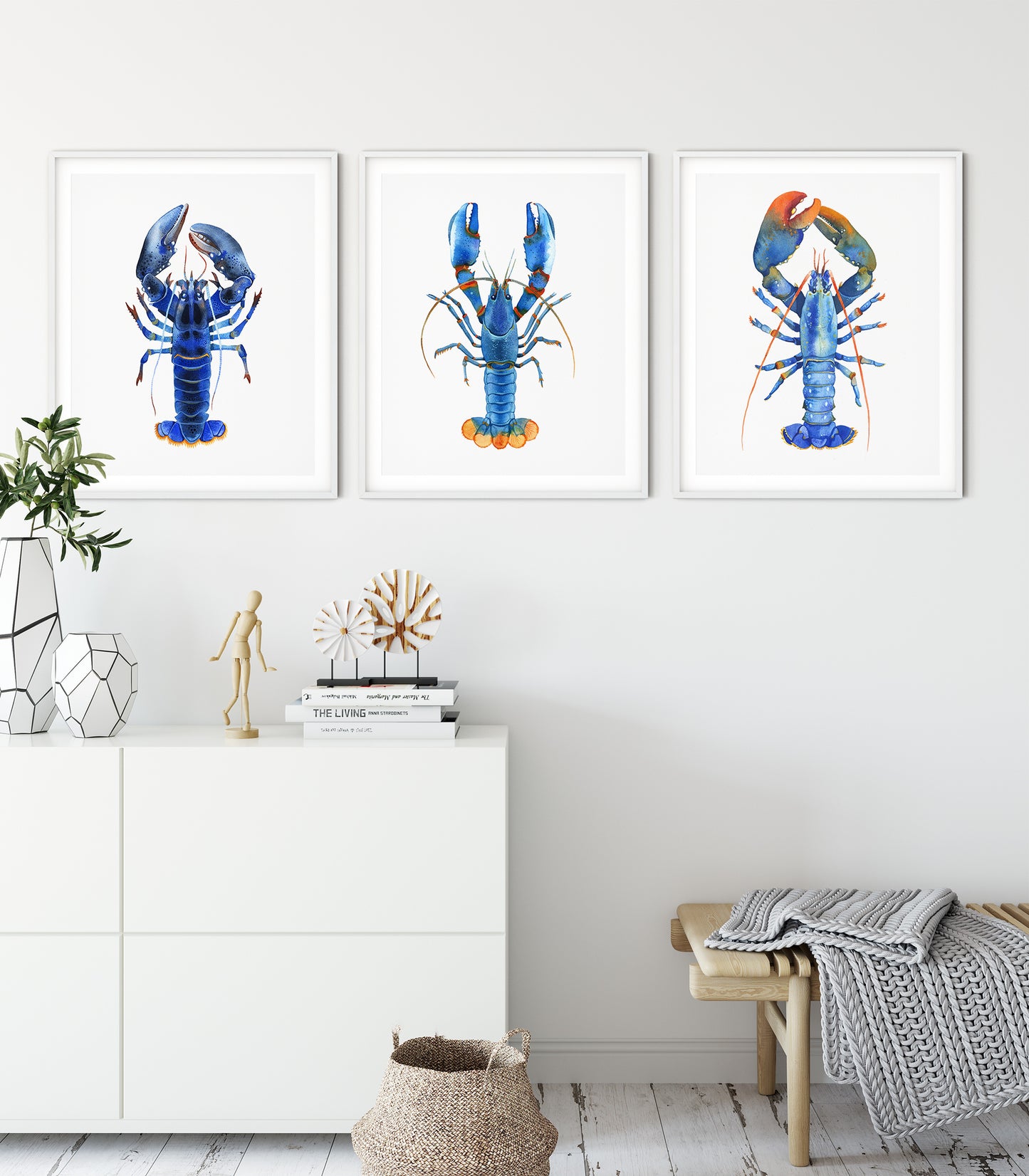 Set of hree framed watercolor lobster prints in blue, teal, and orange tones displayed on a white wall
