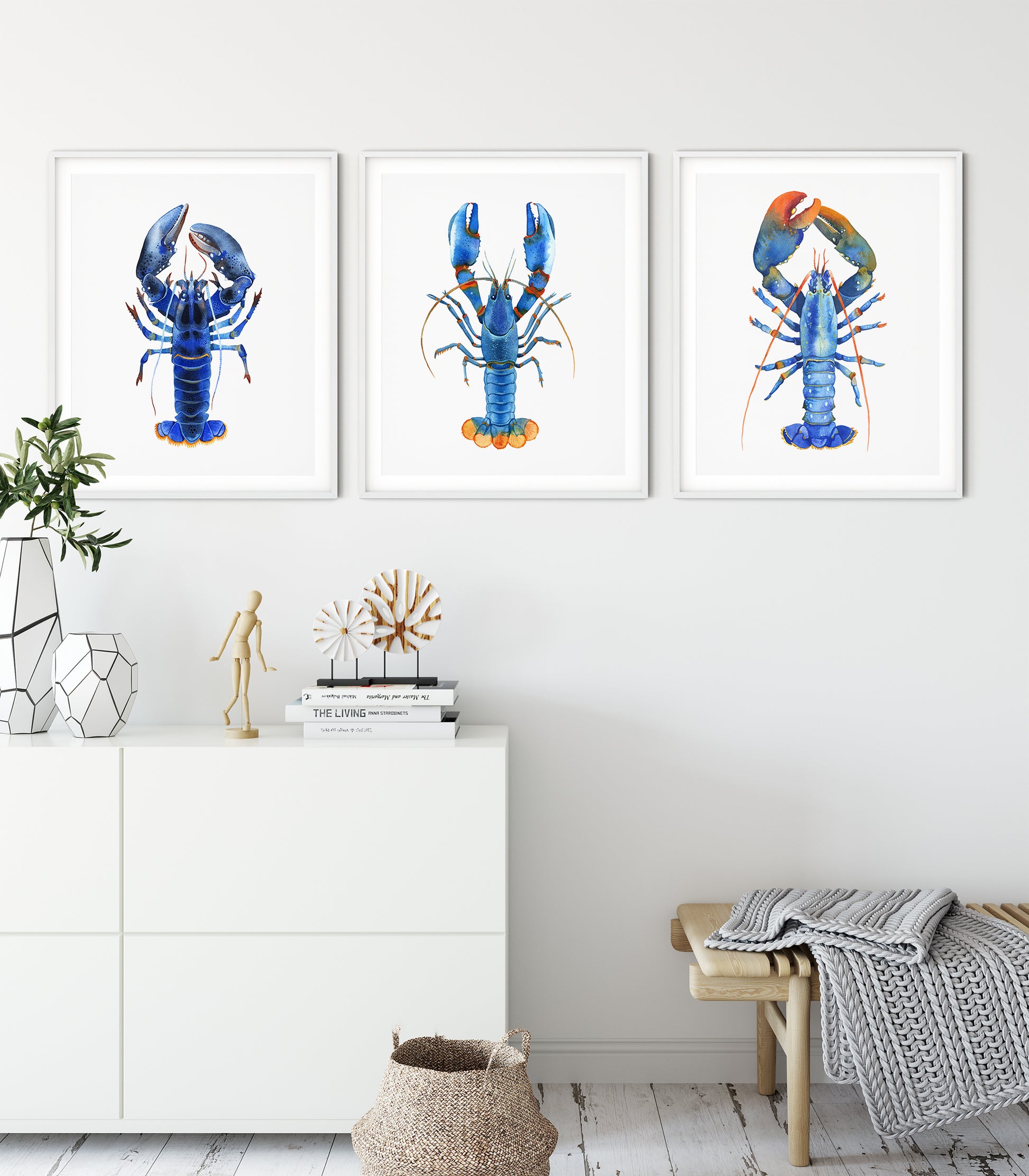 Set of hree framed watercolor lobster prints in blue, teal, and orange tones displayed on a white wall