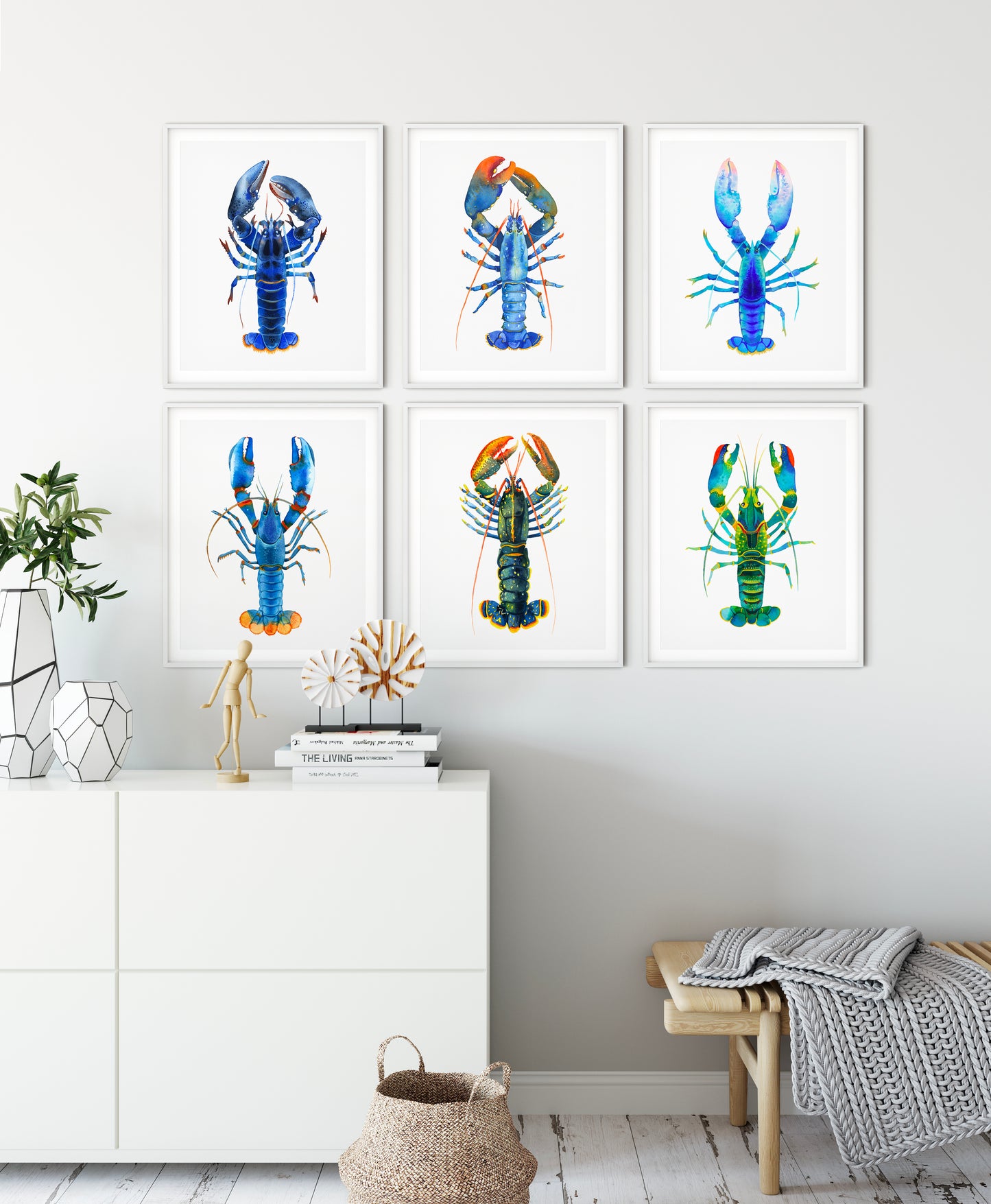 Six framed blue lobster watercolor art prints displayed on a light gray wall above a white cabinet.