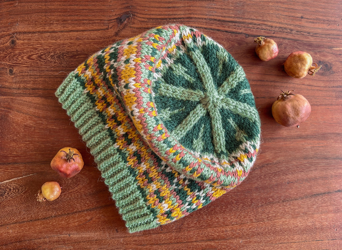 A crown of a hand-knitted hat with a Fair Isle pattern in dark green, sage green, yellow, pink, and beige