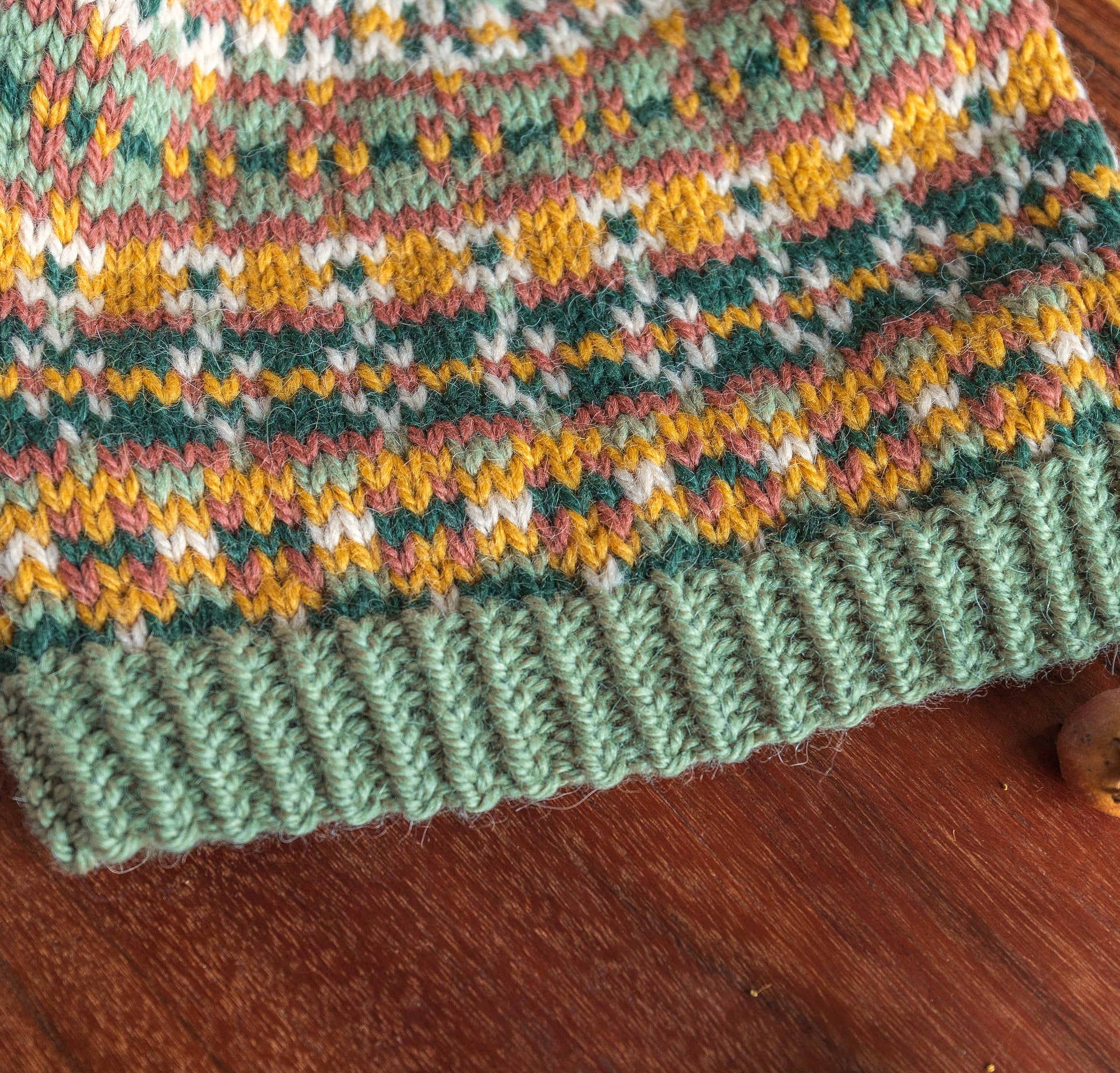 Close-up of a twisted ribbing of a hand-knitted hat with a Fair Isle pattern in dark green, sage green, yellow, pink, and beige