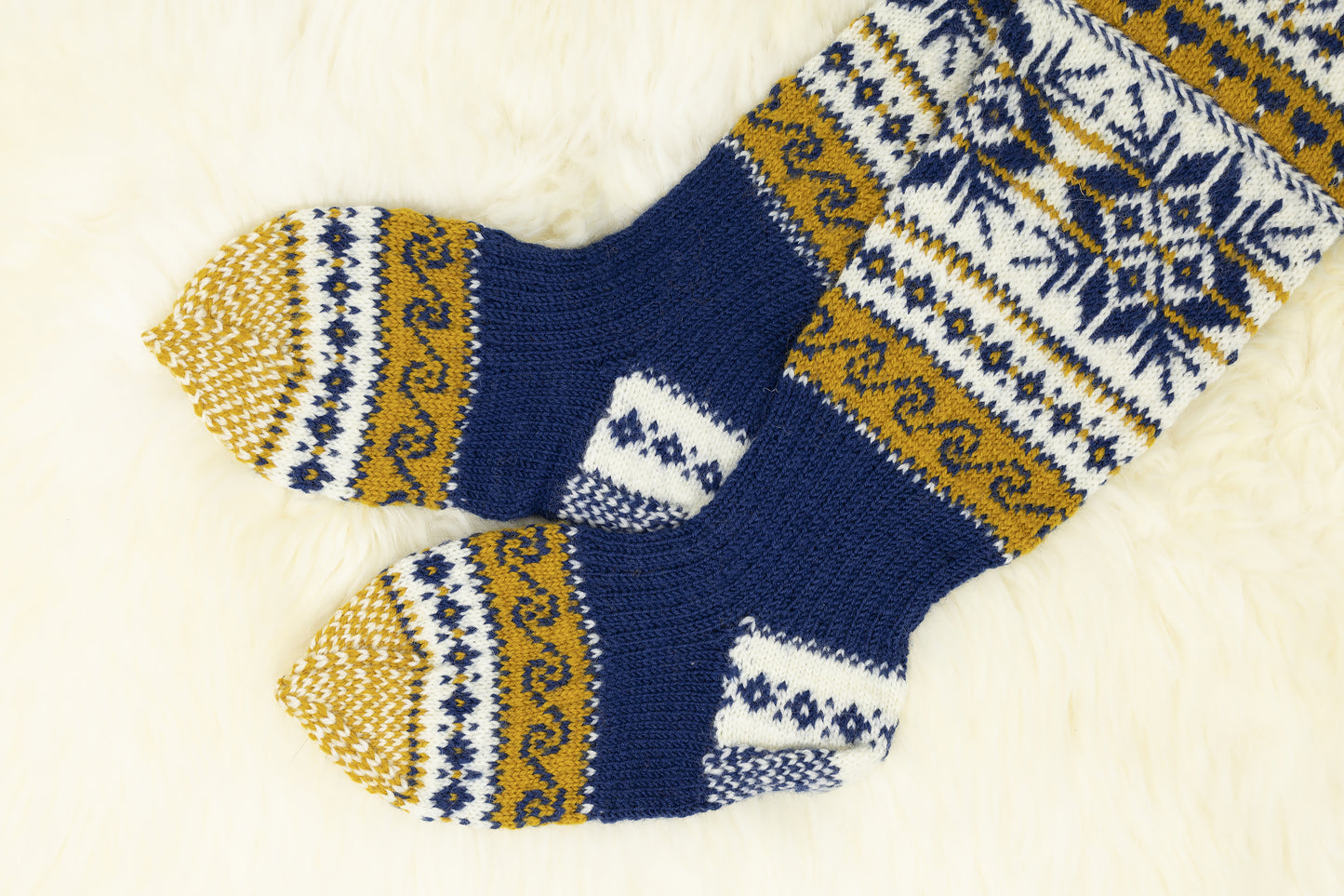 Heels and soles of a pair of hand-knitted Estonian knee-high socks with snowflake and geometric pattern in blue, yellow, and white on a light background