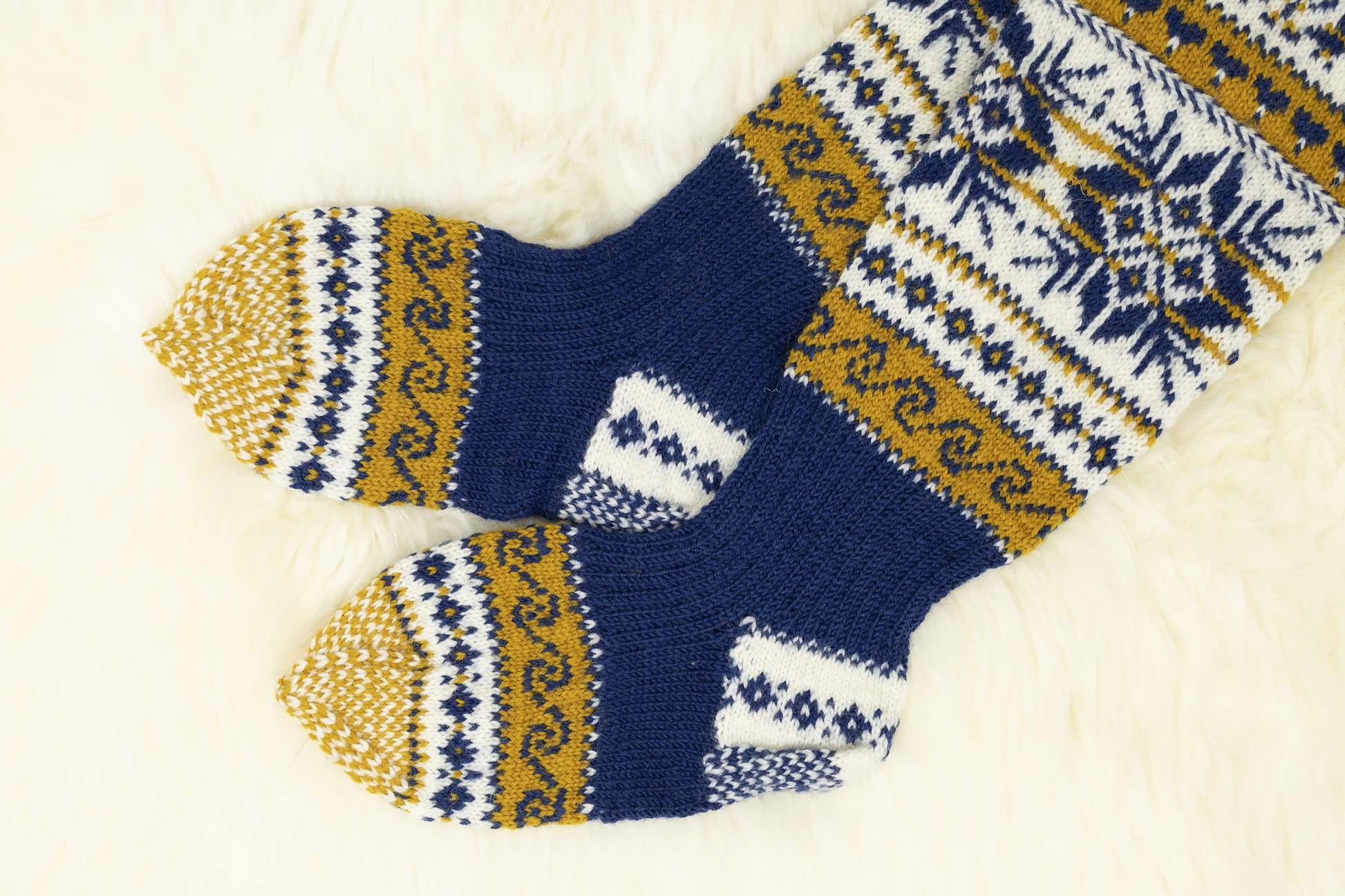 Heels and soles of a pair of hand-knitted Estonian knee-high socks with snowflake and geometric pattern in blue, yellow, and white on a light background