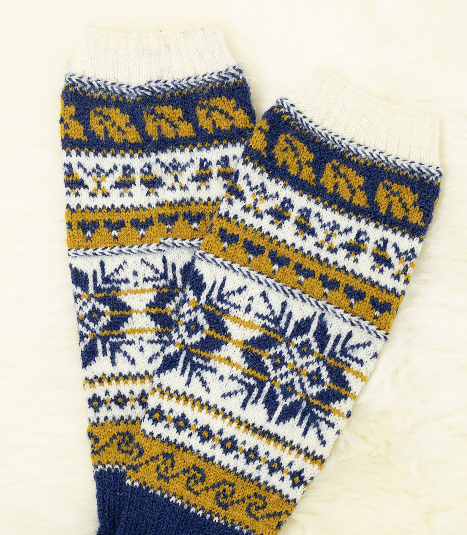 Legs of a pair of hand-knitted Estonian knee-high socks with snowflake and geometric pattern in blue, yellow, and white on a light background