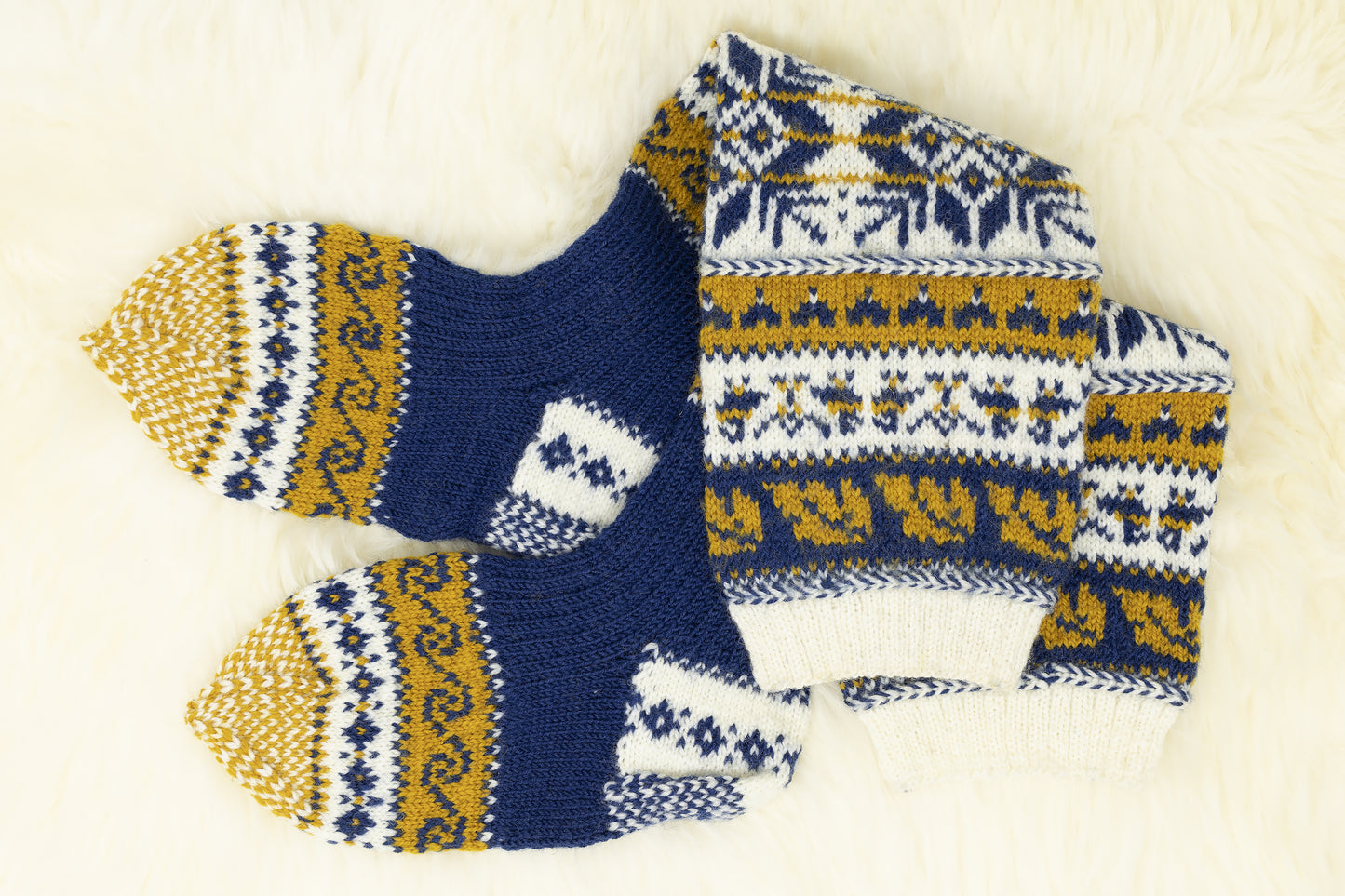 Pair of hand-knitted Estonian knee-high socks with snowflake and geometric pattern in blue, yellow, and white on a light background