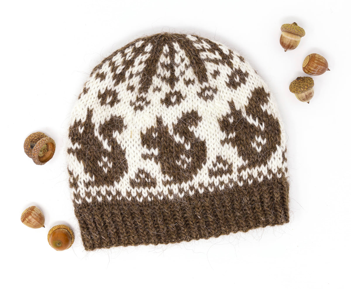 A knitted beanie hat with a brown and off-white Fair Isle squirrels pattern, displayed on a white background with acorns,