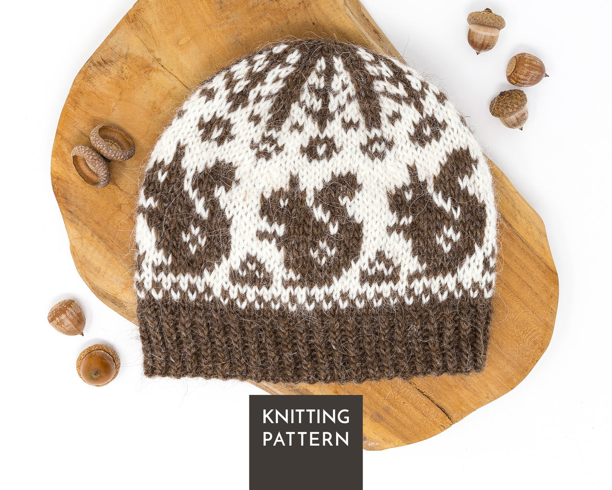 A knitted beanie hat with a brown and off-white Fair Isle pattern, displayed on a rustic wooden slice with acorns, with a 'KNITTING PATTERN' label overlay at the bottom.