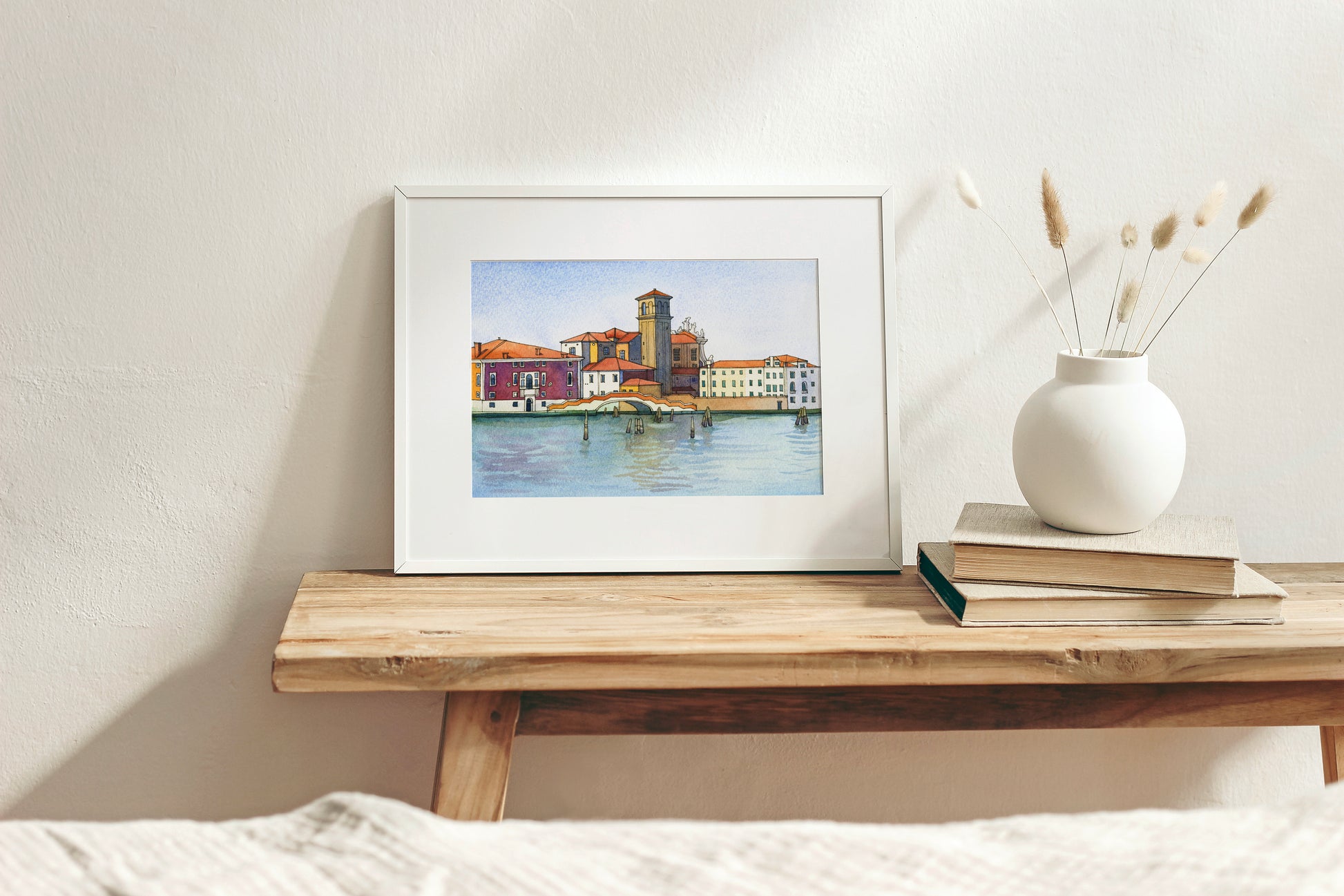 Framed watercolor artwork of Venetian Fondamenta Nova, on a wooden shelf with a vase and books.