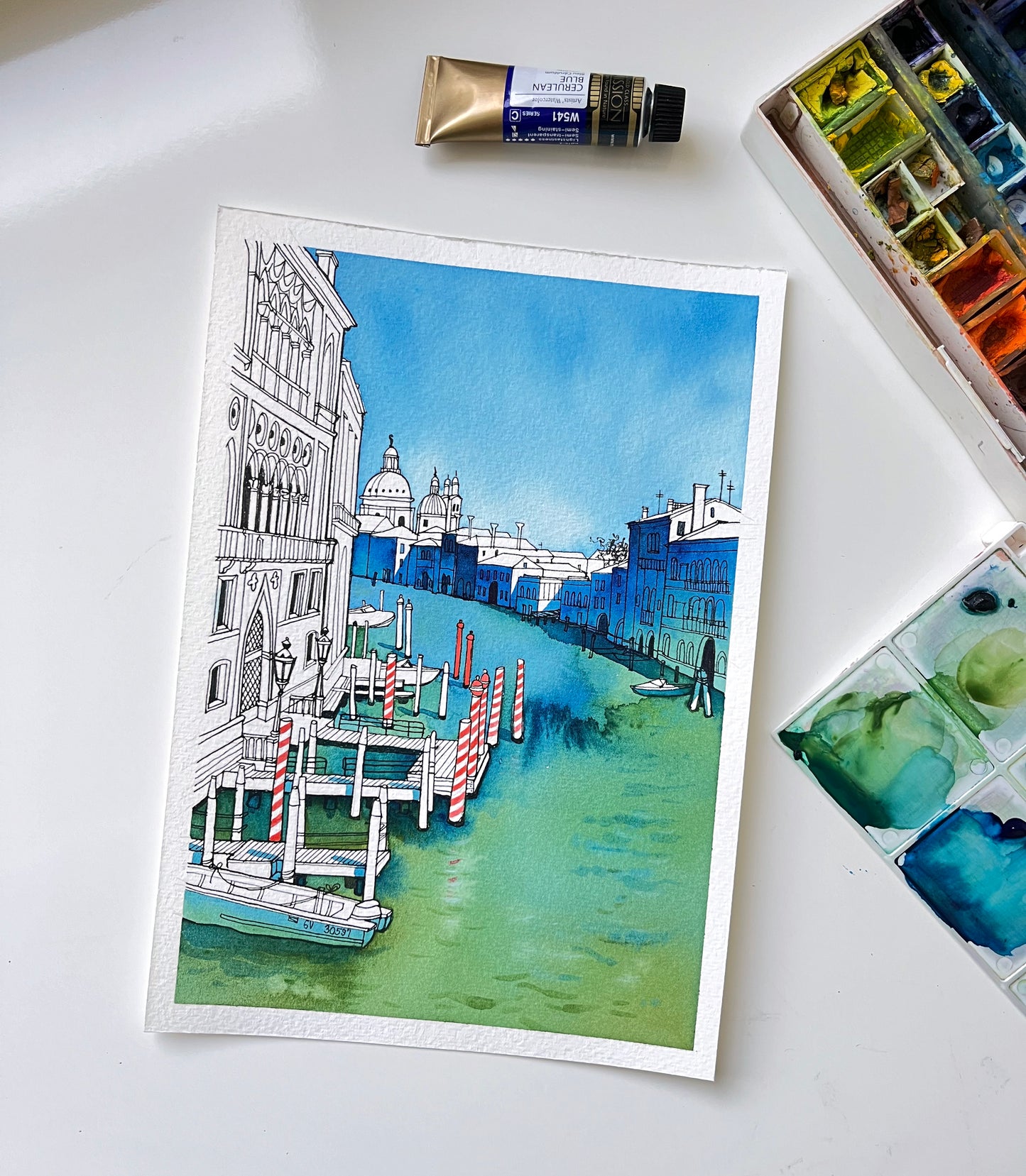 Original watercolor and ink artwork of  Venetian Grand canal viewed from the Accademia Bridge with buildings and boats, accompanied by art supplies.