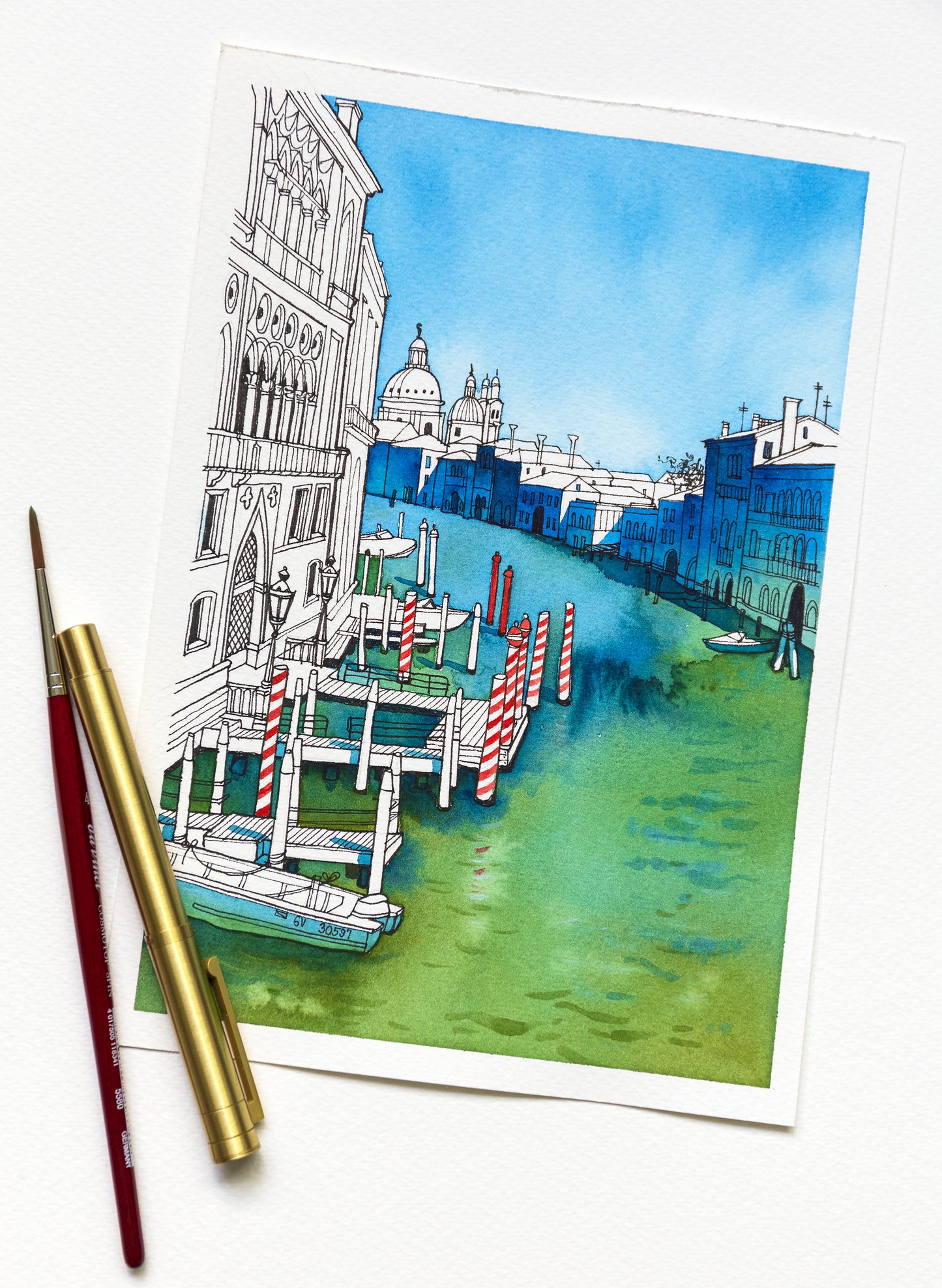 Original watercolor Illustration of a Venetian Grand canal viewed from the Accademia Bridge with gondolas, buildings, and a clear sky, accompanied by paintbrush and pen.
