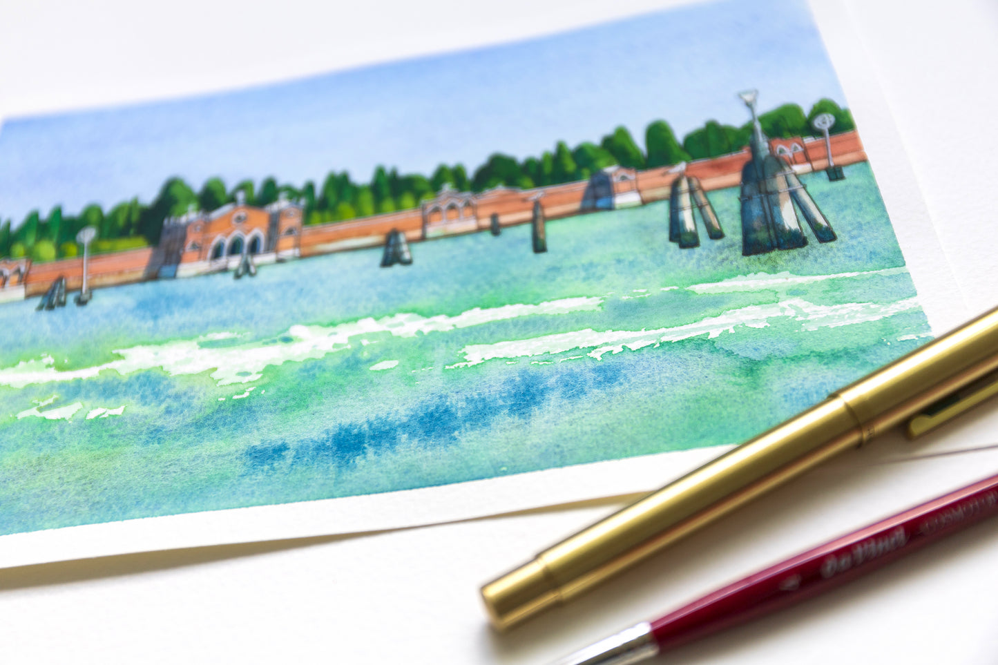 Close-up of original watercolor and ink artwork of San Michele island in Venice, accompanied by two pens.