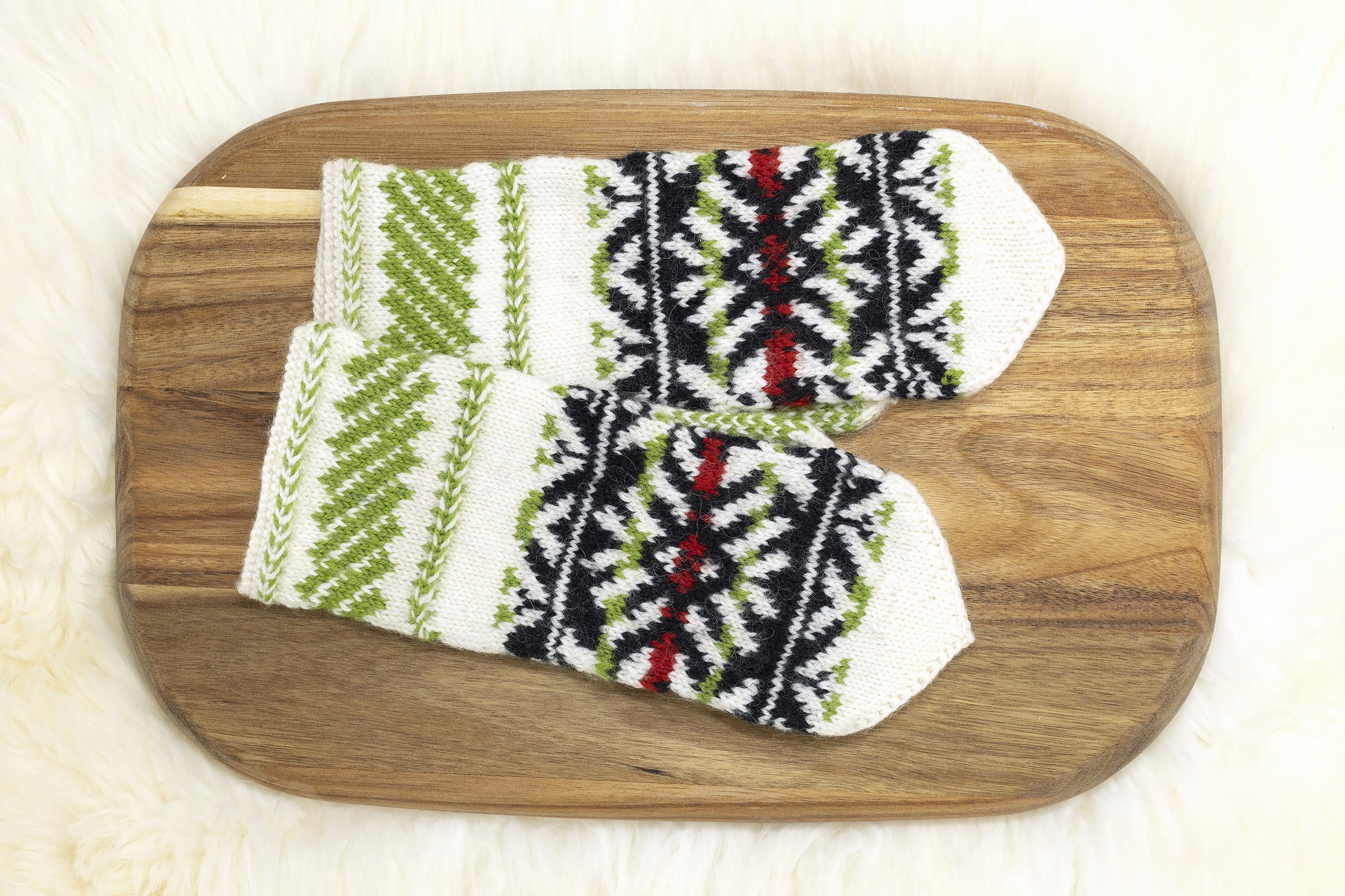 Pair of white, black, green and red hand-knitted mittens in traditonal Estonian pattern a wooden board